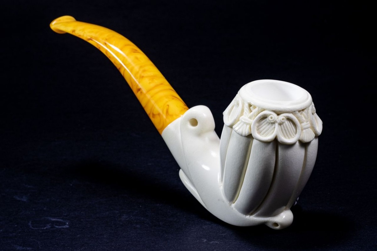 Unique Meerschaum Free Form pipe featuring flowing, sculptural lines and ornate detailing near the bowl, paired with a warm amber stem on a dark backdrop.